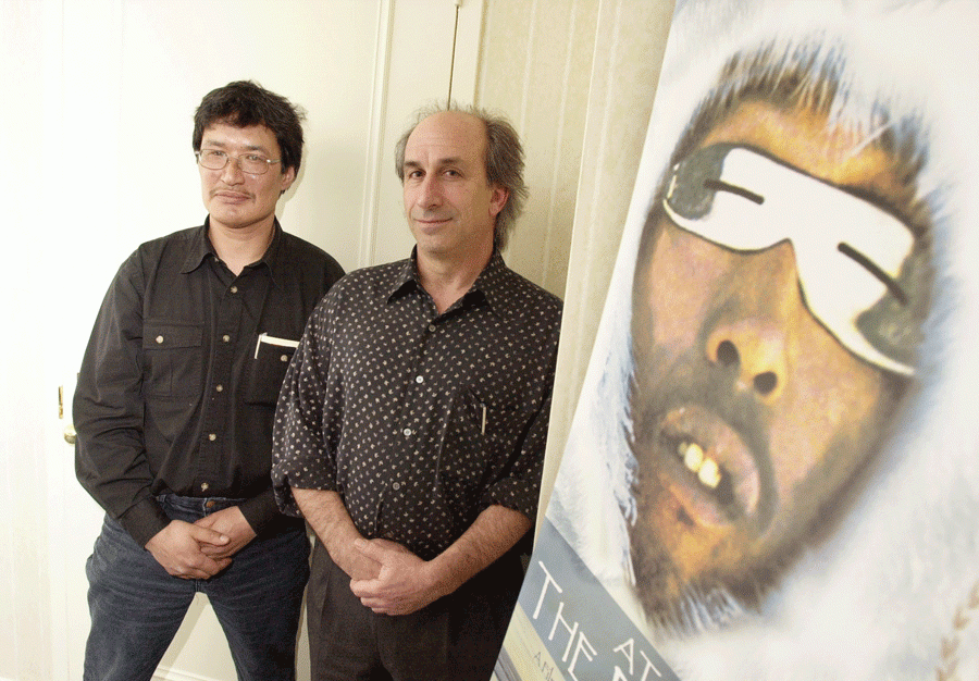 Two INuit men standing in front of a poster of an Inuit celebrity