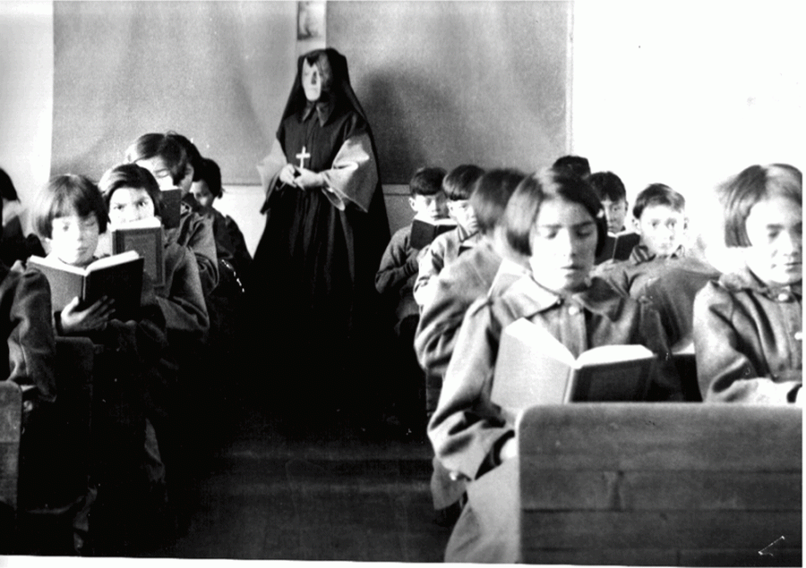 Children in a classroom reading with a nun supervising