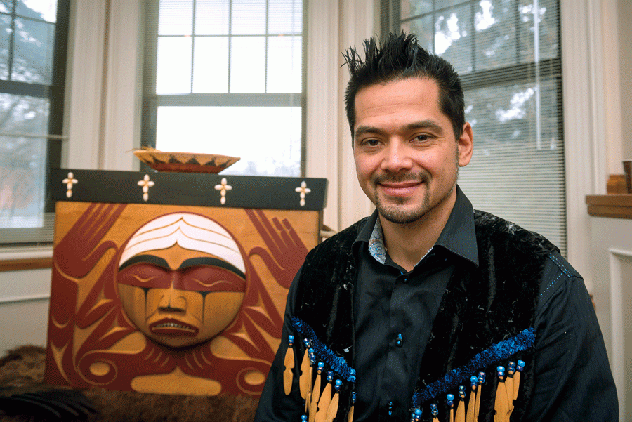 man smiling beside a wooden box with a face carved into it