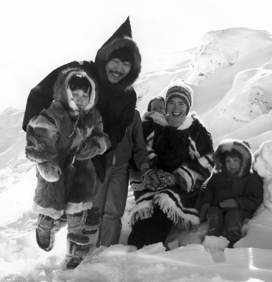 Family of five sitting in snow and smiling