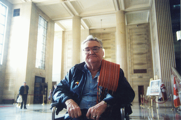 Man with glasses in a wheelchair with scarf over his left shoulder