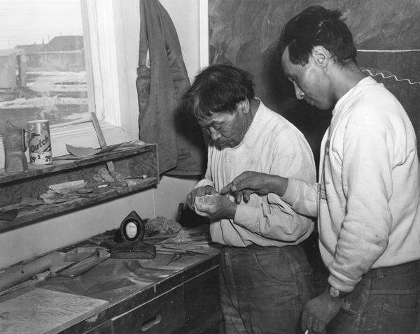 Two men looking at a carving over a table with carving materials