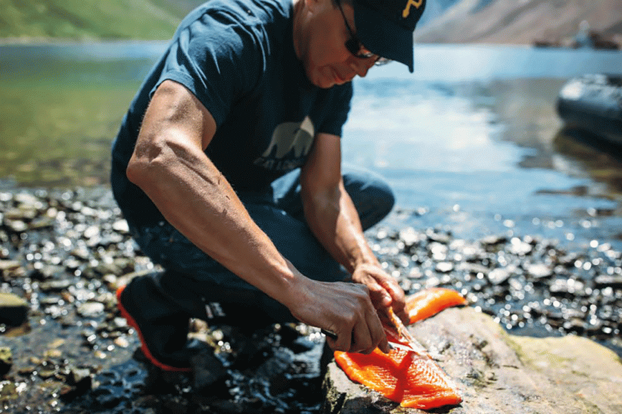 Man kneeling and gutting a fish on the shoreline